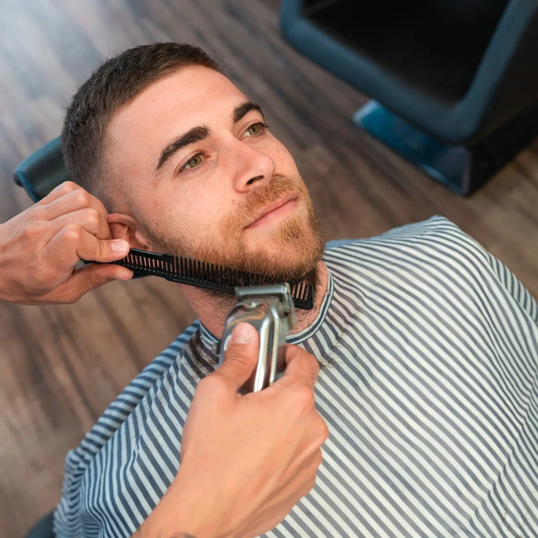 Barber używający maszynki i grzebienia podczas modelowania brody klienta